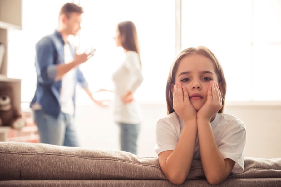 Child sitting in foreground looking distressed while parents argue in background during divorce